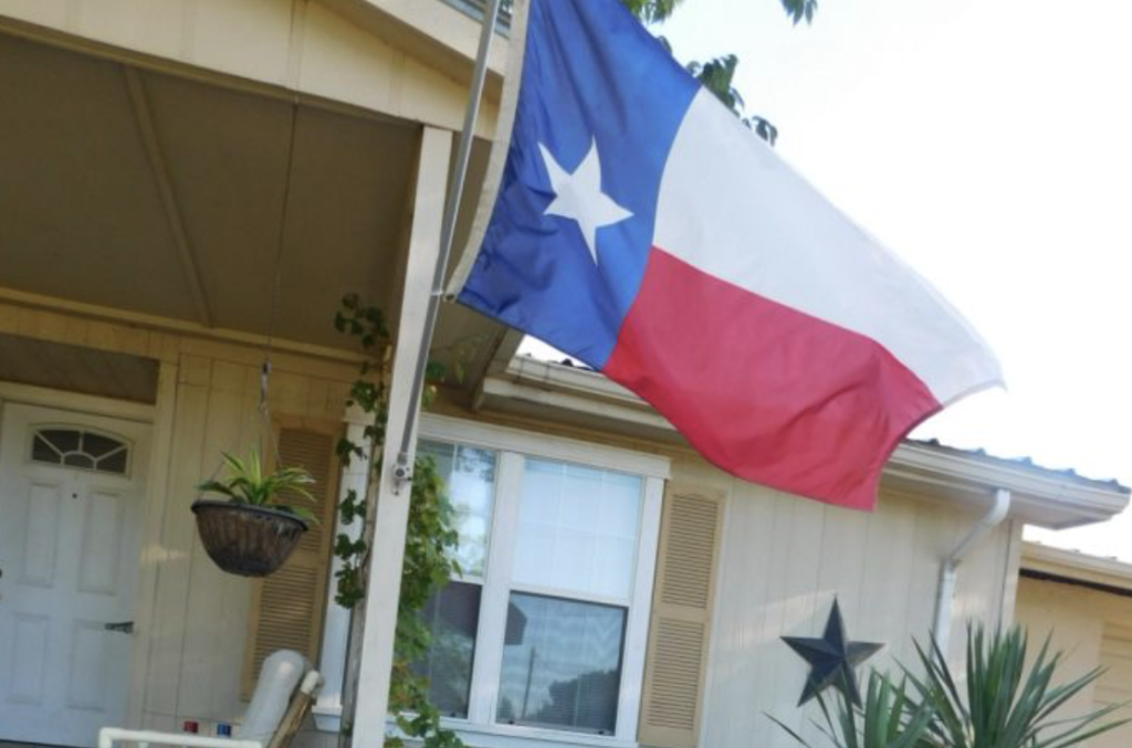 A Texan flag waves in front of a home decorated with native plants